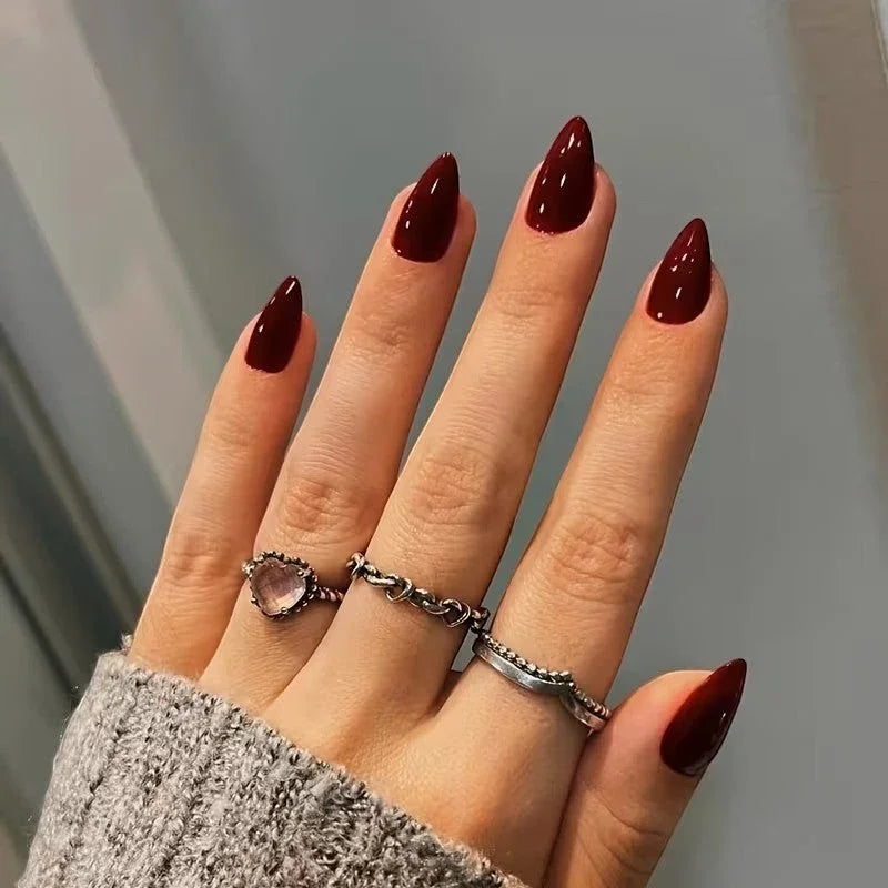 doobysnailsltd deep red almond shaped press-on nails on a hand wearing silver rings